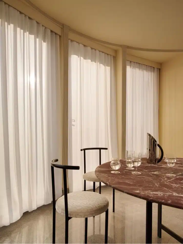 Dining room with large white curtains that follow the curved shape of the glass walls